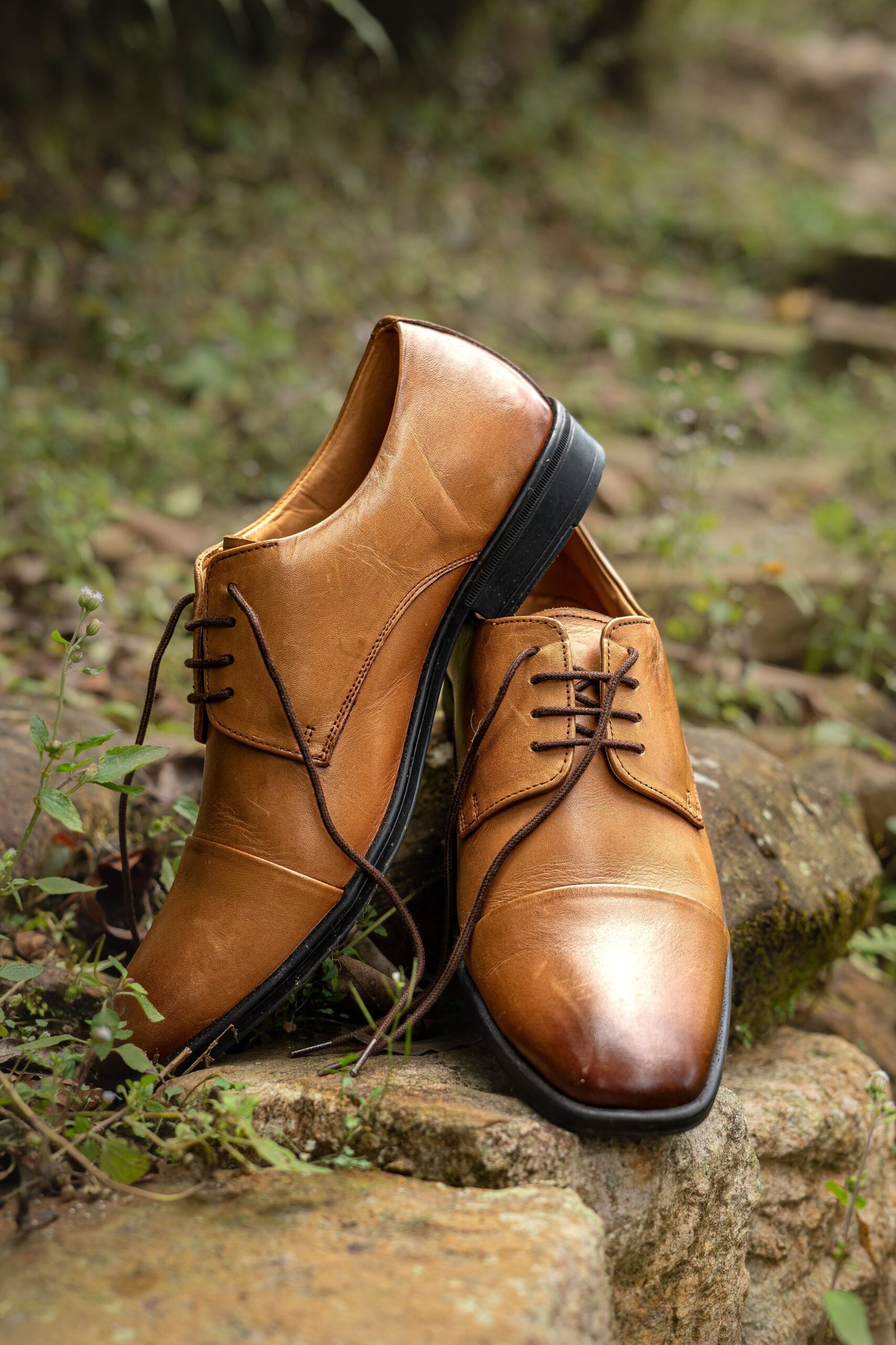 Stylish brown leather formal shoes placed on rocks in a natural setting.