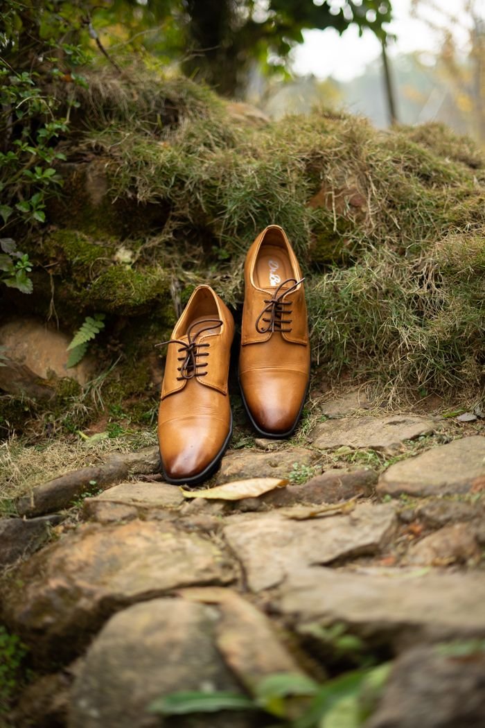 Elegant brown leather shoes placed on a rocky path outdoors, showcasing style and craftsmanship.